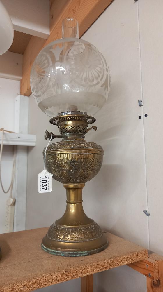 A Victorian oil lamp with embossed brass base and original etched shade. COLLECT ONLY.