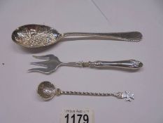 A silver plate fruit spoon, a pickle fork with silver handle and a spoon with a 1776 coin bowl.