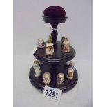 Fifteen Royal Crown Derby thimbles on a thimble stand with pin cushion.