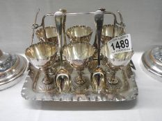 A silver plate six piece egg cup stand with spoons.