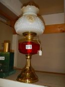 An oil lamp with brass base, red glass font and complete with shade, COLLECT ONLY.