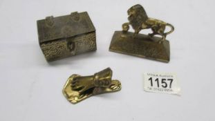 A brass casket, a brass hand paperclip and a brass lion paperweight.