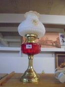 An oil lamp on a brass base with a red glass shade and floral shade. COLLECT ONLY.