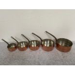 Set of five copper graduate saucepans with metal handles.