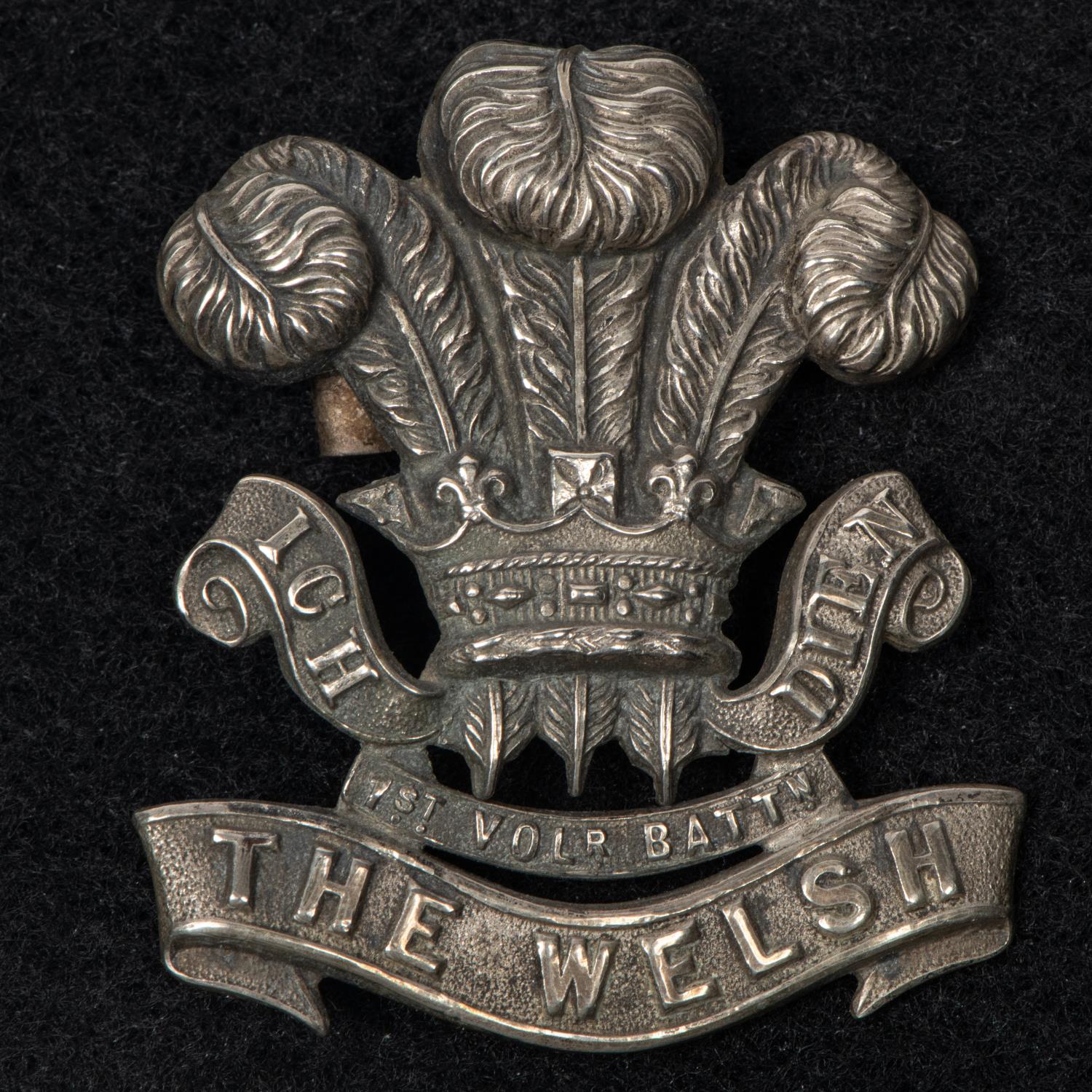 A white metal cap badge of the 1st Volunteer Battalion the Welsh Regiment, with blades. GC (