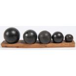 Five small cast iron cannon/grapeshot balls, mounted on a wooden base in descending order of size,