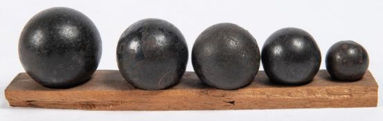 Five small cast iron cannon/grapeshot balls, mounted on a wooden base in descending order of size,