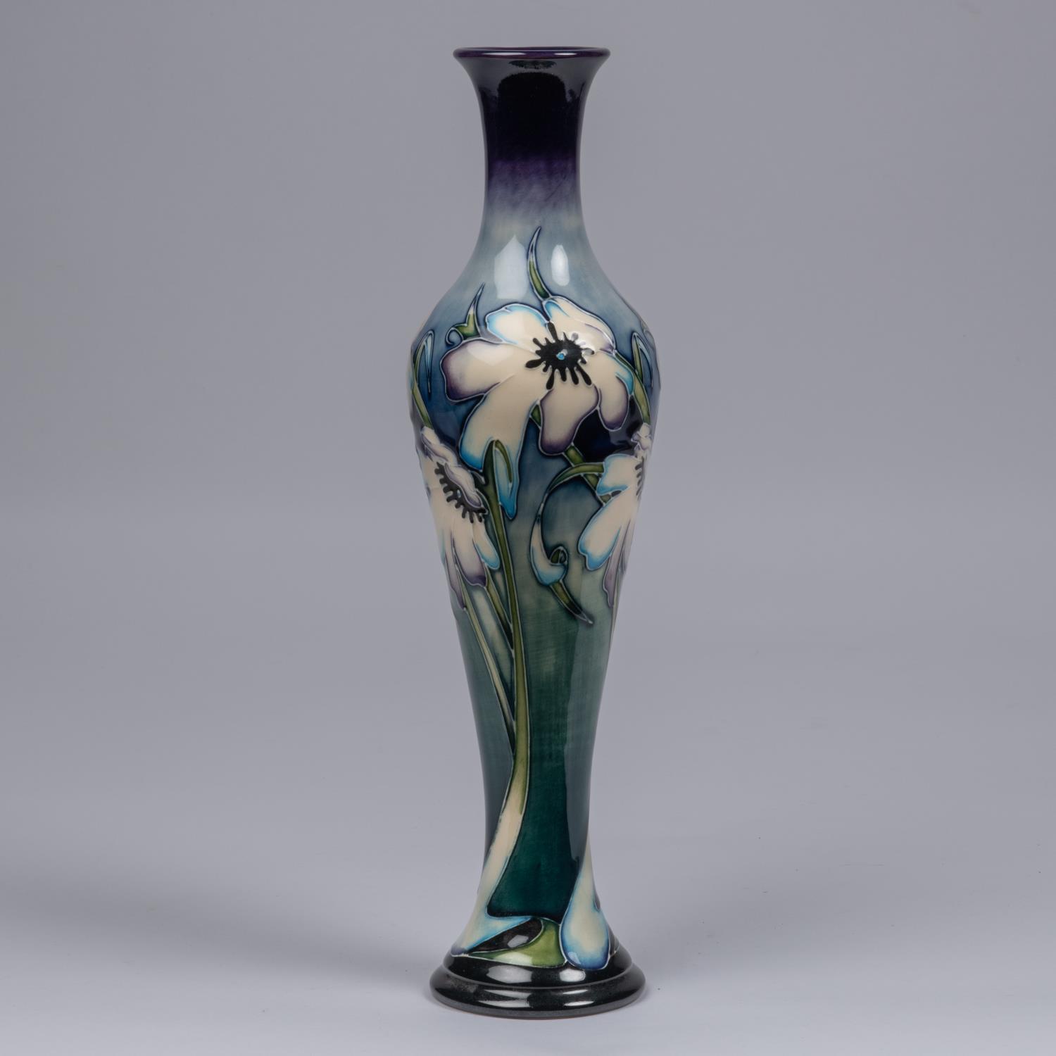 A Moorcroft pottery slim vase. Blue tinged white flowers on a graded green and blue ground. Marks to