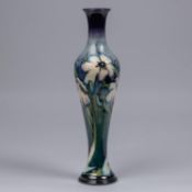 A Moorcroft pottery slim vase. Blue tinged white flowers on a graded green and blue ground. Marks to