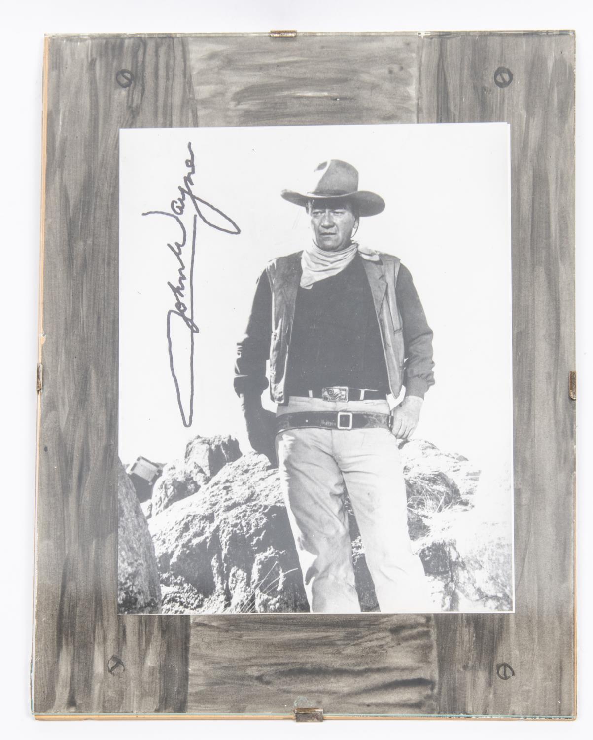 An autographed photograph of John Wayne, 10" x 8", in Western costume, signed vertically. In mount