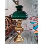 A vintage brass paraffin lamp with funnel and green glass shade.
