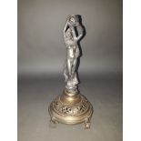 A pewter and brass candle holder, depicting a female figure holding an urn above her head, the