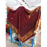 An Arts & Crafts bed throw, maroon background with flower pattern and tassels.