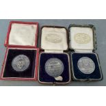 Three white metal sports medals in boxes, one with hallmarks for silver.