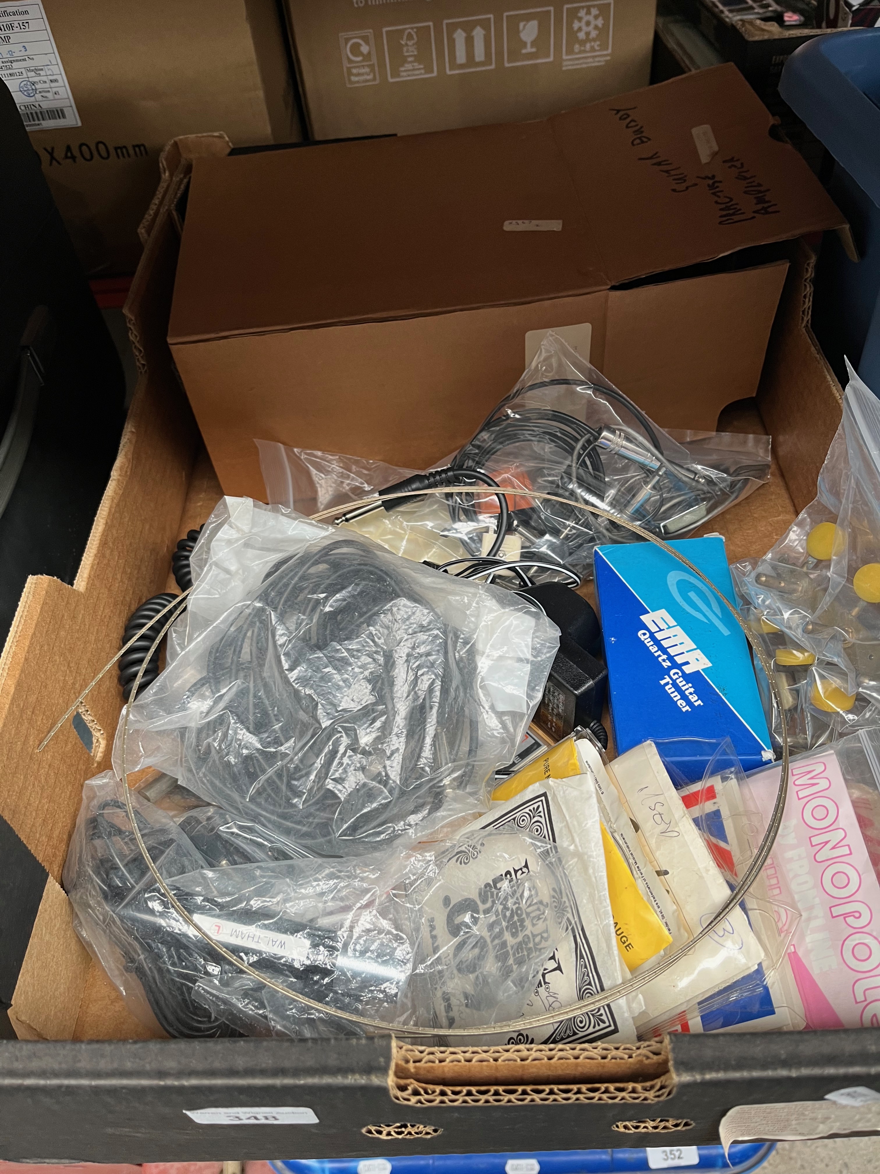 A box of guitar and banjo accessories to include strings, tuners and a practice amplifier etc.