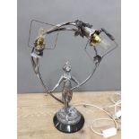An Art Deco chrome table lamp modelled as a semi nude female figure holding a wreath of flowers,
