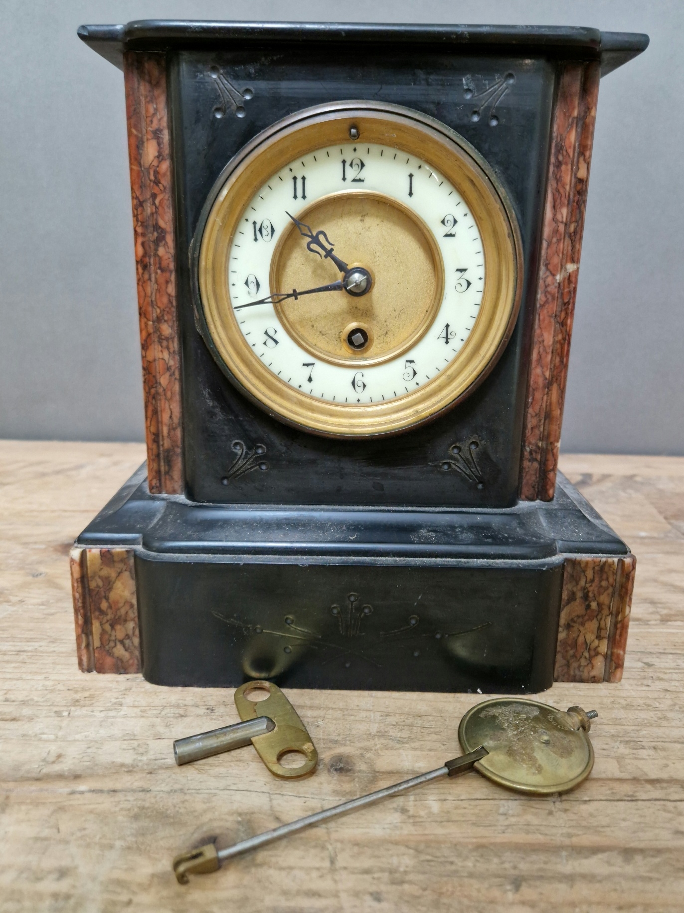 A black slate and marble mantle clock, with gilt and enamel face, pendulum and key.