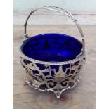 A George V silver sugar basket, swing handle, pierced bowl stood on four feet, blue glass liner,