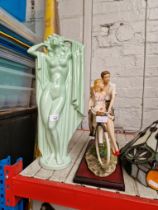 Two pottery figures, lady and a couple on a bicycle mounted on a plinth