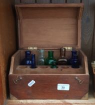 An early 20th century oak case containing a number of coloured glass medicine bottles.