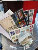 A tub of assorted first day covers and loose mint stamps