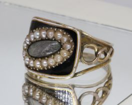 A Georgian black enamel and split pearl mourning ring, central oval hair panel surrounded by