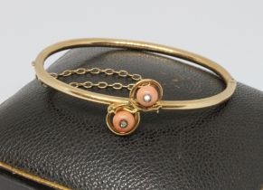 An antique coral and diamond bangle, two coral beads set with a rose cut diamond and surround by a