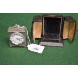 Silver cased travelling clock with top carrying handle and engine turned decoration, standing on
