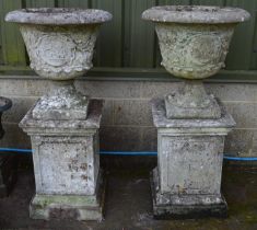 Pair of weathered garden urn having cherub and foliate decoration on three piece square plinth stand