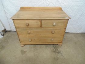 Stripped pine chest of two long and two short drawers with raised back and standing on bun feet -