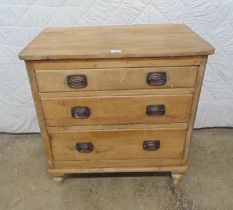 Stripped pine chest of three long graduated drawers with brass handles, standing on turned feet -