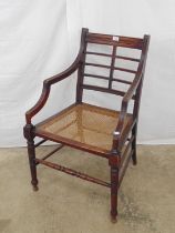 Mahogany elbow chair in the manner of EW Godwin with bar back over cane work seat, standing on