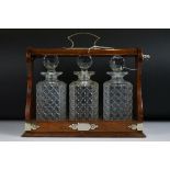 Edwardian oak three bottle tantalus with silver plated mounts and carry handle, three matching cut