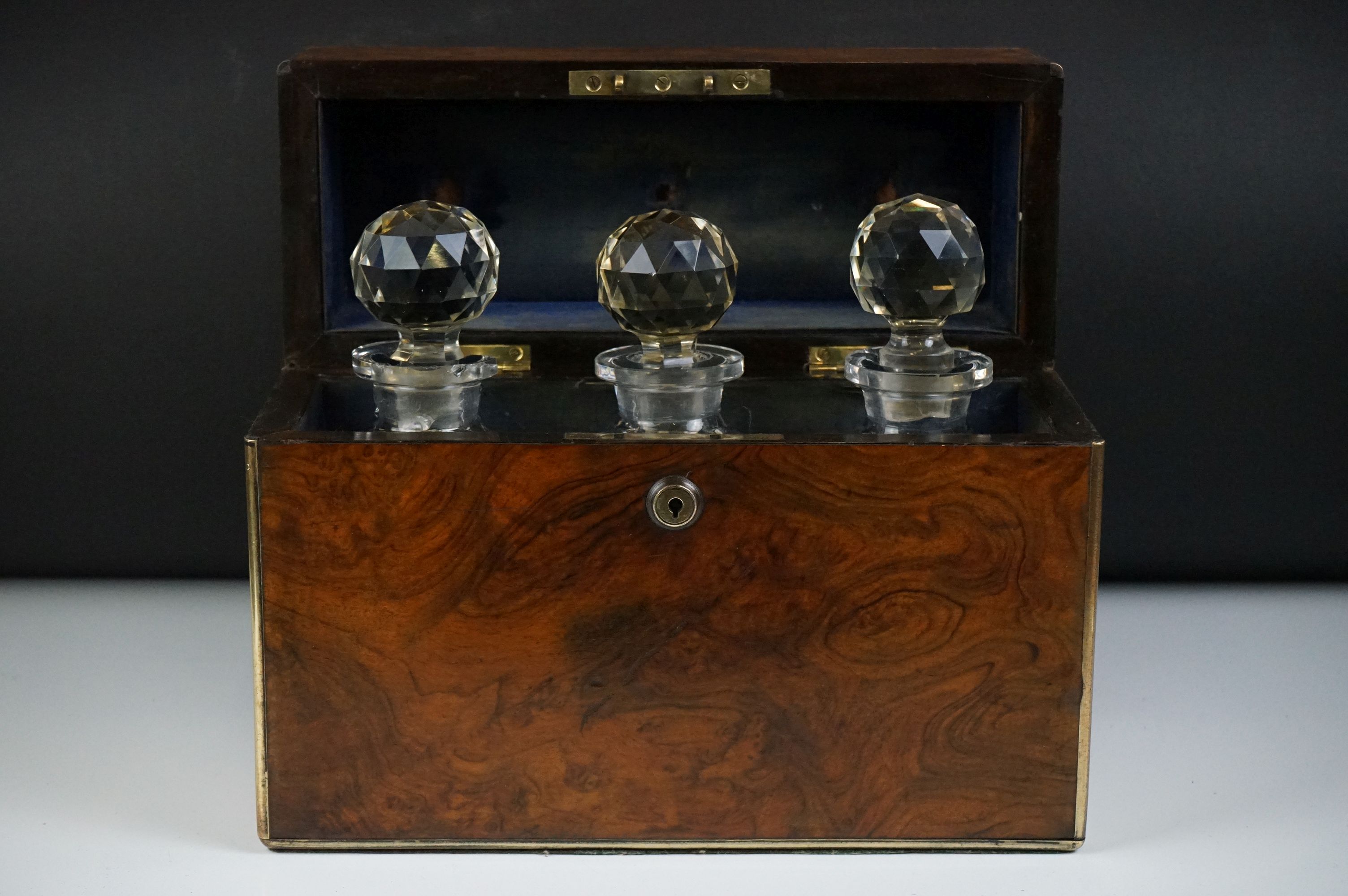 Victorian burr walnut brass-bound three bottle tantalus, containing three matching cut glass