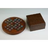 A carved wooden solitaire board together with a box of vintage marbles.