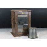 A wooden smokers cabinet with beveled glass door, brass furniture and pewter tobacco jar.