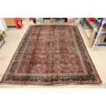 Red Ground Wool Rug with stylised floral pattern within a blue ground border, 288cm x 376cm