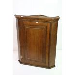 Early 19th century Oak Hanging Corner Cupboard, the single panel door opening to two shaped shelves,