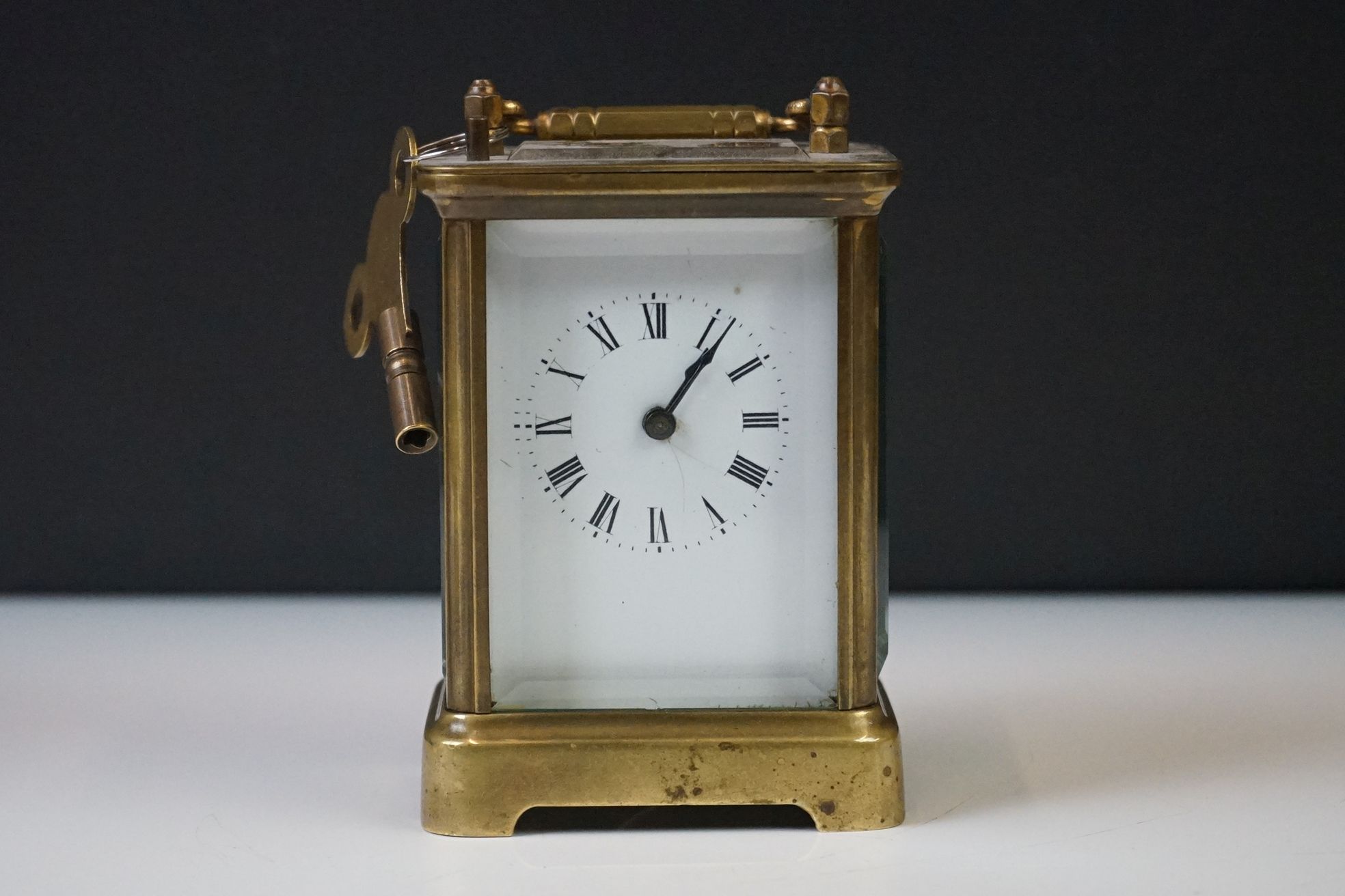 A brass cased carriage clock with beveled glass panels and white enamel dial, complete with key.