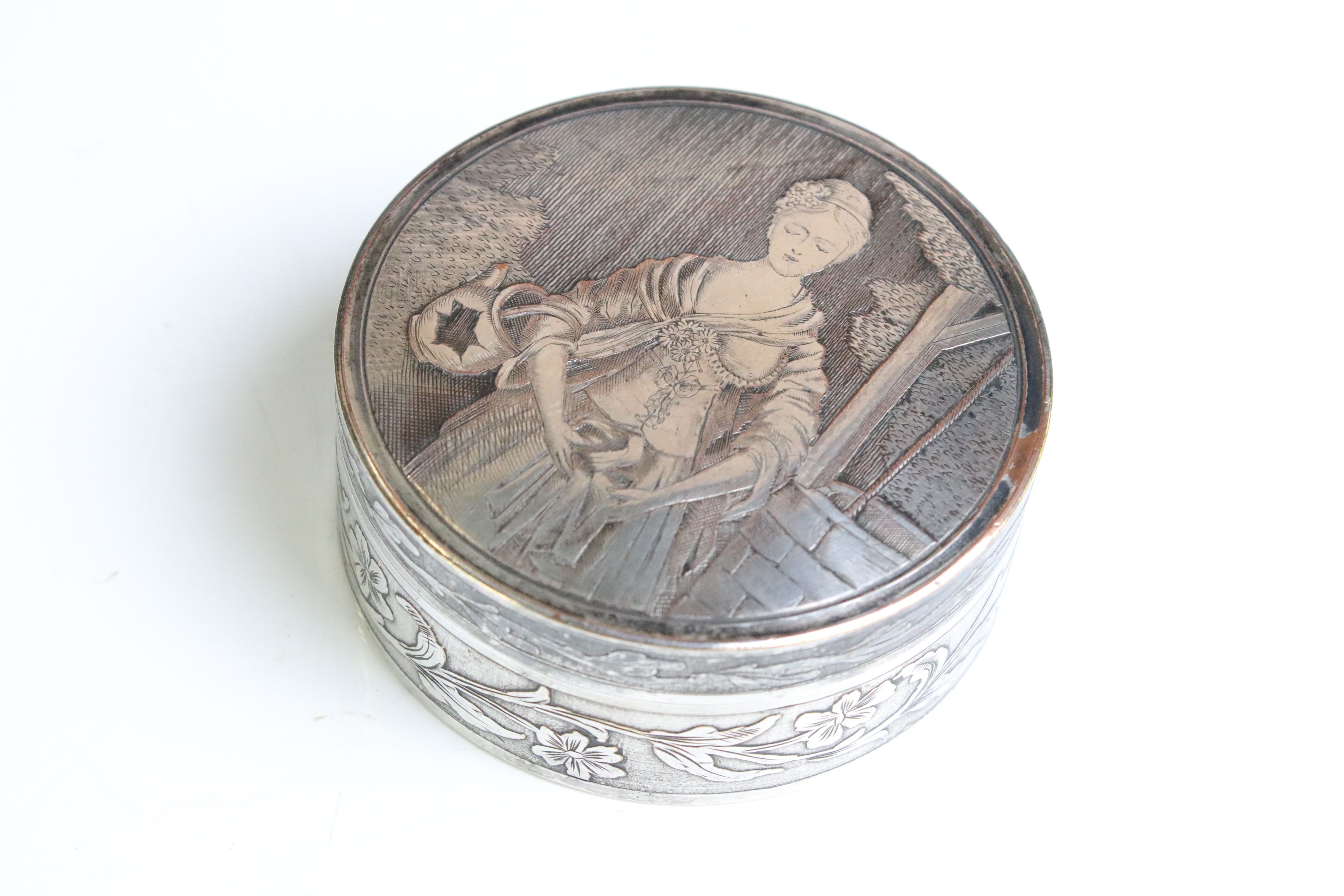 A vintage white metal powder jar with figural decoration to the lid and foliate decoration to the