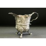 19th century Irish silver jug raised on three hoof feet, repoussé floral and scroll decoration,