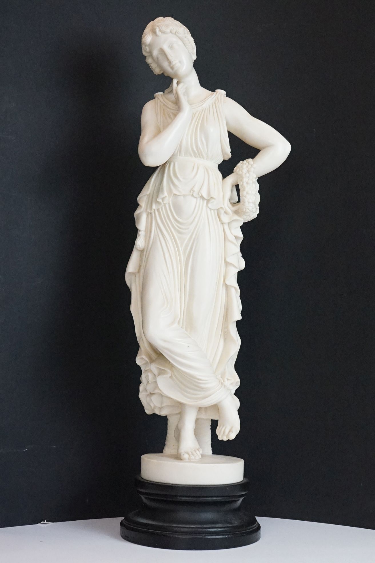 Resin sculpture of a classical maiden, in a pensive pose, raised on a wooden pedestal base. Measures