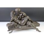 Resin & composition erotic sculpture of a couple embracing upon a bed, raised on four metal legs.