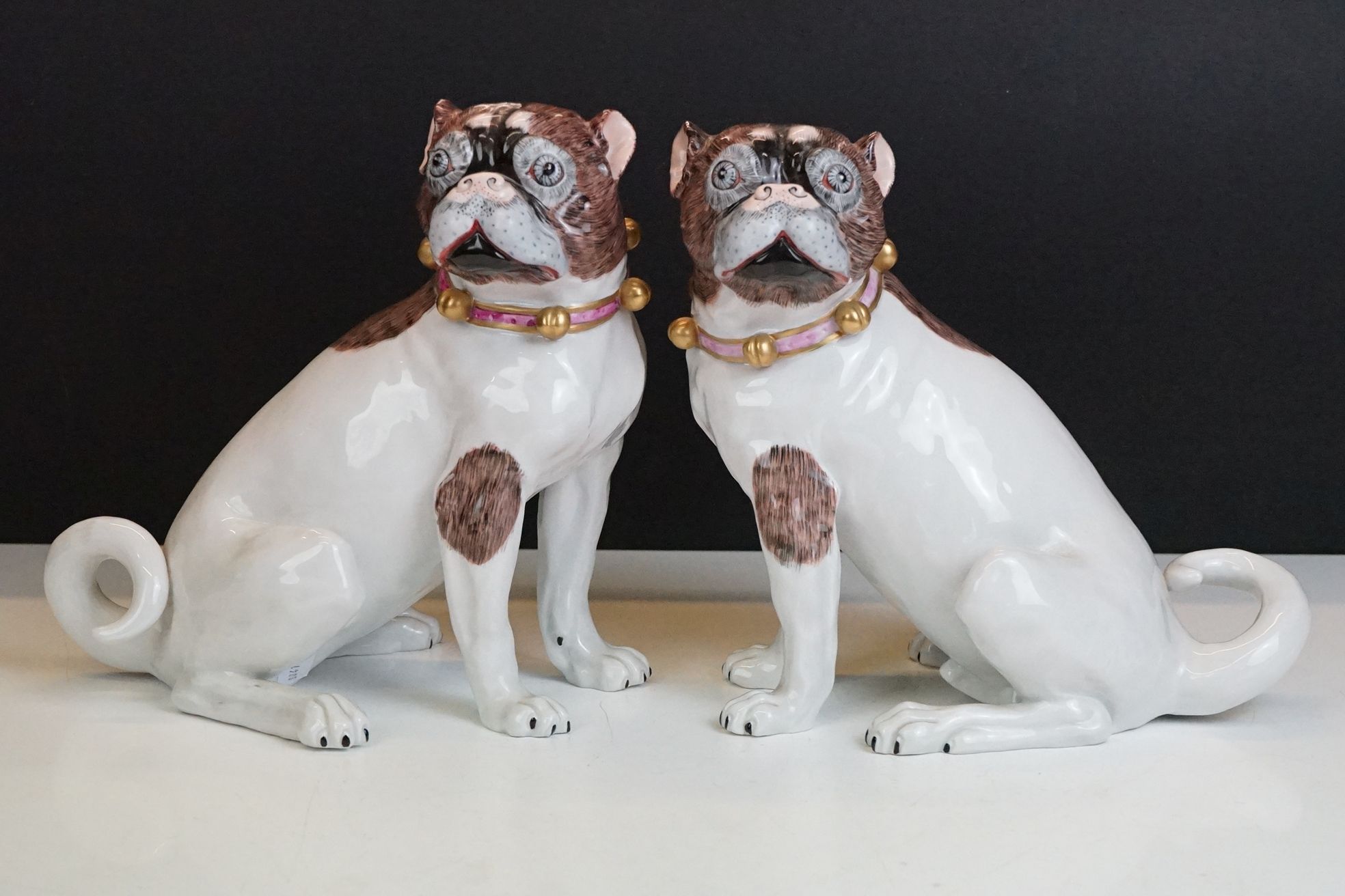 Near pair of 20th Century Dresden seated Pug figures, wearing gilt & pink collars, with hand painted