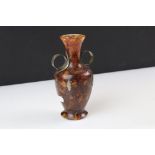 An ornamental twin handled vase, made with amber chips set in resin, stands approx 15cm in height.
