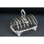 William IV silver seven bar toast rack raised on four scroll feet, the handle with cast foliate