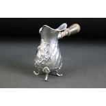 Edwardian silver milk jug with turned wood side handle, repousse floral decoration on a spiralling