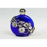 A blue glass scent bottle with white metal floral decoration.