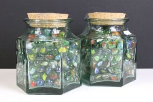 A large collection of mixed marbles contained within two glass jars.