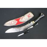 A Kukuri knife with decoratively engraved blade and red velvet and white metal covered sheath.